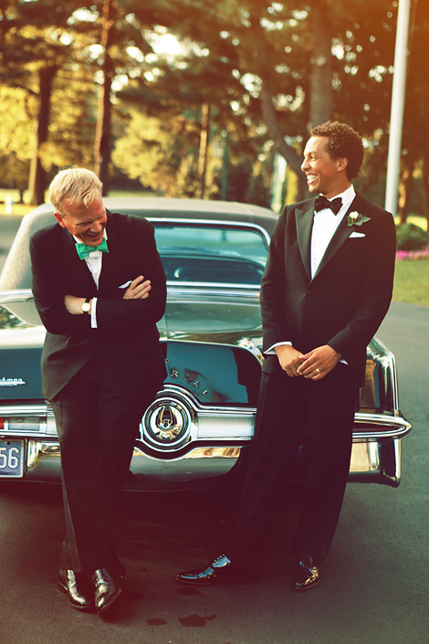 The groom and a friend lean against the Imperial vintage car on the sunny wedding day